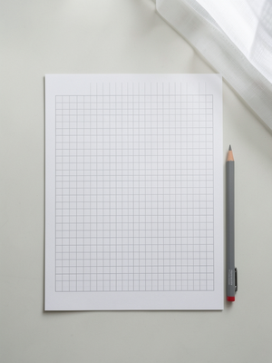 Overhead flat-lay photograph of Japanese stationery on a desk surface,. A minimal close study of Japanese grid paper on 