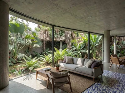 Open-plan living room where an entire wall dissolves into a tropical garden, fer