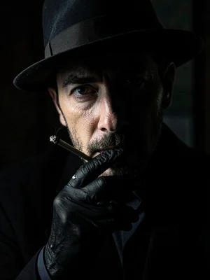 Man in fedora lighting cigarette, match the only light source, revealing half hi