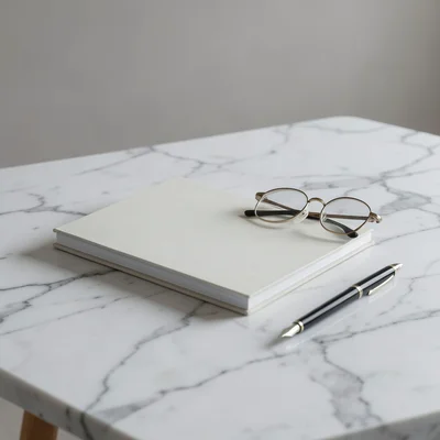 Stack of notebooks, fountain pen, and reading glasses on a marble desk surface