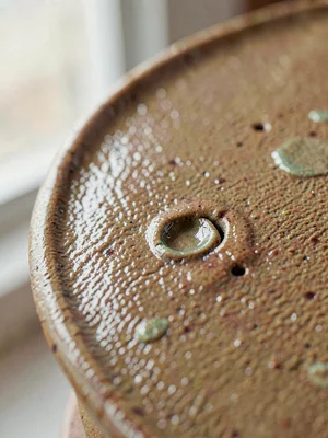 Salt-glazed stoneware curve, pebbled skin punctuated by a deep hand-pressed dent