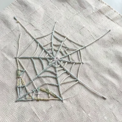 Hand-stitched spiderweb on linen, geometric thread pattern, corner placement