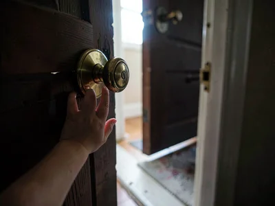 Child's hand reaching for an oversized brass doorknob, the door cracked open rev