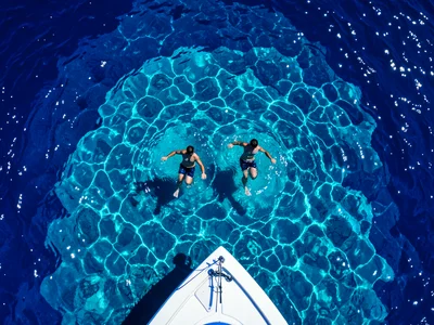 Two people treading water in open ocean, seen from a boat above, the deep blue s