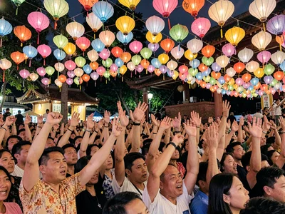 Temple festival crowd compressed into wave of paper lanterns and raised hands, i