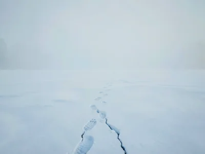 Snowfield broken by a single line of footprints leading into the void, the print