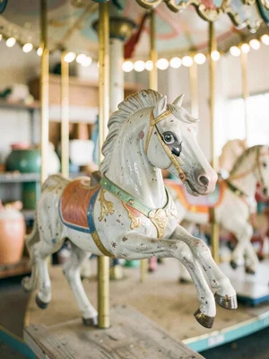 Paint-chipped carousel horse in storage, one glass eye cracked, gilt faded to gr