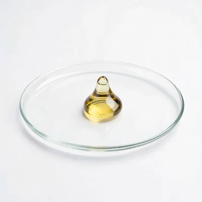 Clean studio macro of a single drop of golden oil suspended on a glass plate