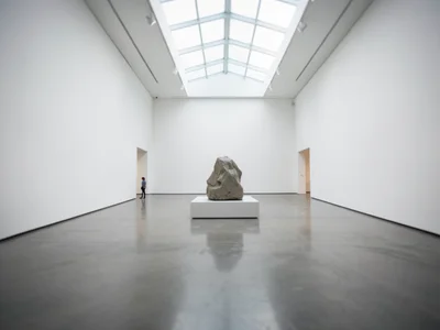 A contemporary art gallery: white walls, concrete floor, a single large sculptur