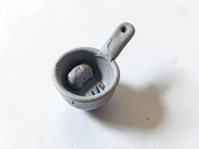 Upturned putty-grey coffee scoop with a slumped handle and thumb dents inside th