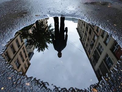 Pedestrian silhouette reflected in rain puddle, dark figure walking through inve