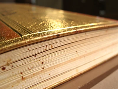 Gilt-edged Bible top view, gold leaf reflecting warm light, thin gold lines betw