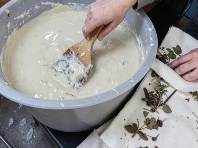 A hand stirring pulp in a large plastic vat, fibres visible in the cloudy water