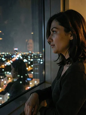 A woman looking out window at night, her reflection overlaid with city lights