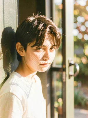 Teenager leaning against a screen door, mesh pattern casting shadows on her face