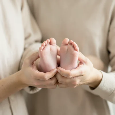 Mother's hands cupping baby's feet, soft focus, warm tones, intimate