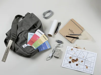 The contents of an architect's messenger bag arranged on a drafting table — a sc