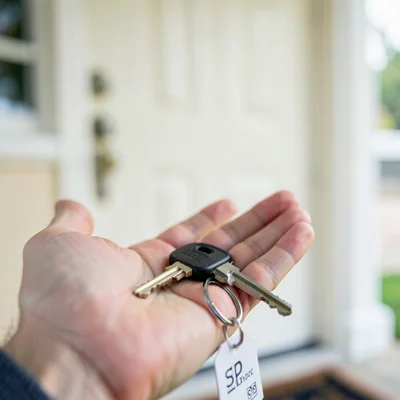 House key sharp in palm, new front door soft blur behind, keychain still has rea