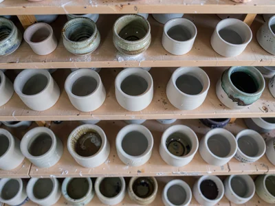 An overhead view of a pottery studio shelf — rows of bisque-fired pieces waiting