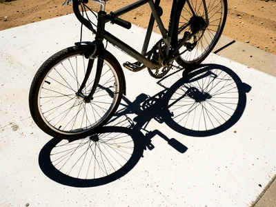 A bicycle locked to a rack casting its shadow onto white concrete in harsh noon 