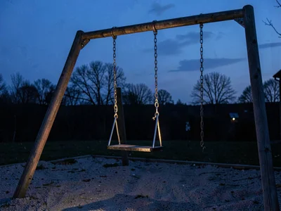 Empty playground swing still moving at blue hour, chain catching last light