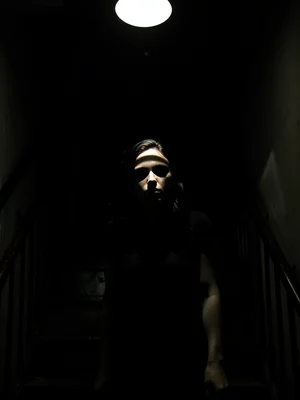 Woman descending staircase, single overhead light creating stripe across her eye