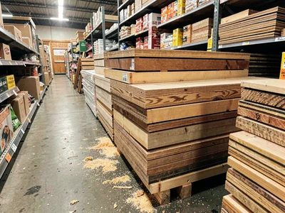 Lumber section, stacked boards showing grain variety, sawdust on concrete floor,