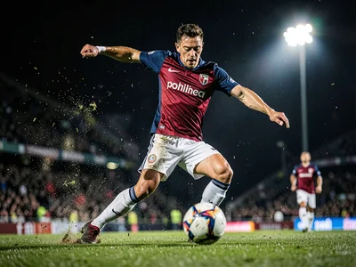 Soccer player striking the ball with perfect form, grass flying, evening floodli