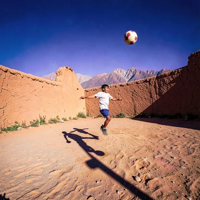 High altitude photograph, thin mountain air, A child kicking a football on a dir