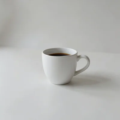 Minimalist photography of a single white coffee cup on a plain matte surface, soft natural window light, clean shadows, 