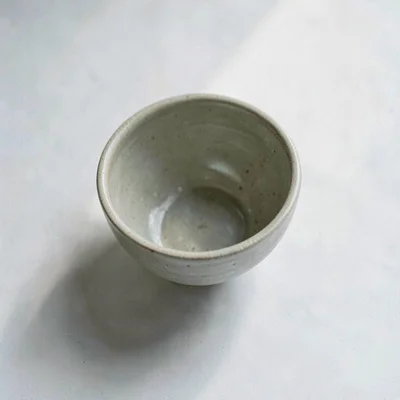 A single ceramic tea bowl viewed from above, soft sheer light pooling inside the