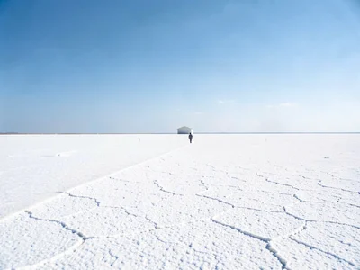 Single figure on salt flat, horizon line cutting frame in half, nothing but whit