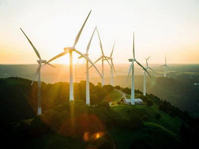 Wind turbines on a ridge at sunset, golden light on white blades, green landscap