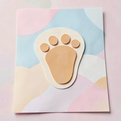 Layered papercraft of a tiny baby footprint in cream and ochre paper layers