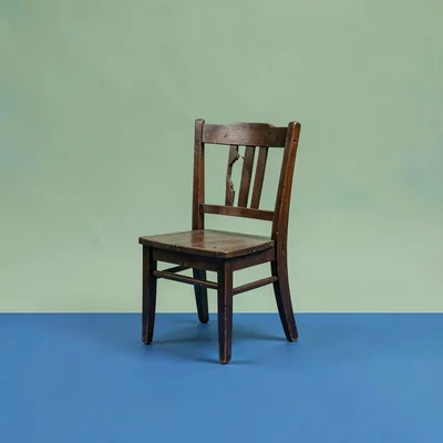 Color-block hero of a broken wooden chair silhouette on a sage-green backdrop, c