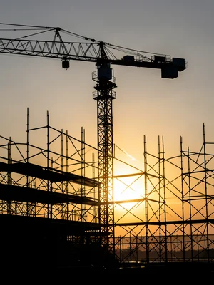 Construction crane silhouette containing sunrise through scaffolding, double exp