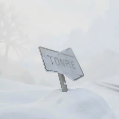 Tilted road sign poking through snow drift, lettering blurred to nothing, the ro