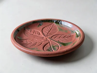 A hand-built slab dish with impressed leaf patterns, fired in earthenware red