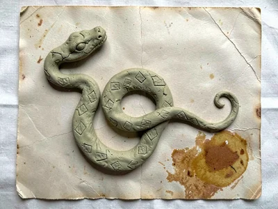 Coiled pressed-clay snake with diamond markings, head at the upper left corner, 