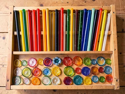 Glass rod color inventory — dozens of colored cane lengths sorted by hue in wood