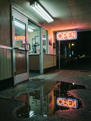 Neon sign reflected in rain puddle outside diner