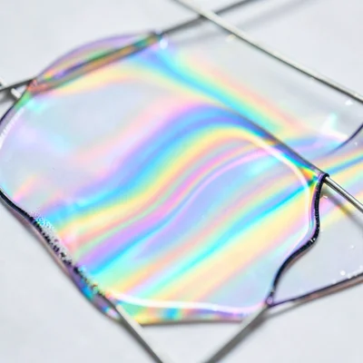Soap film on a Möbius strip wire frame, continuous surface with flowing iridesce