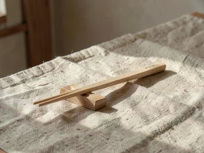 One handcarved wooden chopstick rest of pale beech sitting alone on slubby oatme