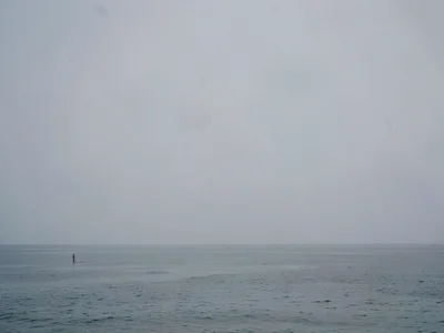 Lone swimmer dot in upper corner of calm grey ocean expanse