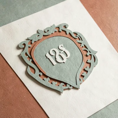 Papercraft composition of a layered paper-cut foundation crest across cream pape