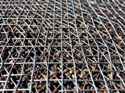 Woven wire with accumulated debris, mesh partially blocked by trapped particles,