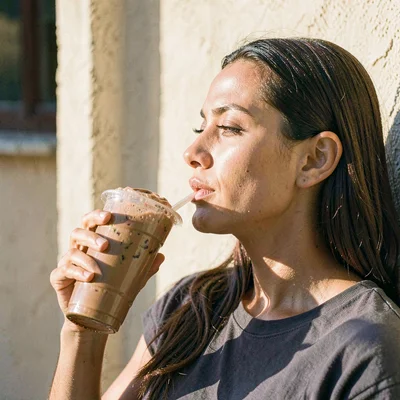 Editorial of a model's profile drinking a brown shake against a sunlit wall