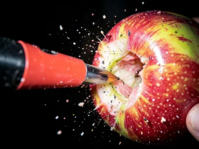 Bullet piercing apple with entry wound visible and flesh just beginning to separ