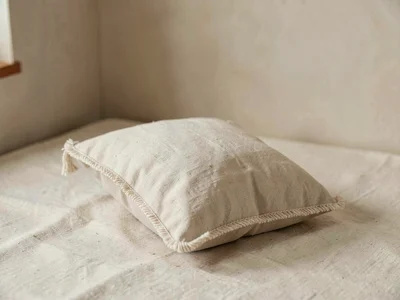 A single small pillow upholstered in undyed linen with corded edges resting on c
