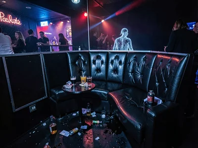 Empty nightclub booth at 4am, spilled drinks catching the still-running lights, 